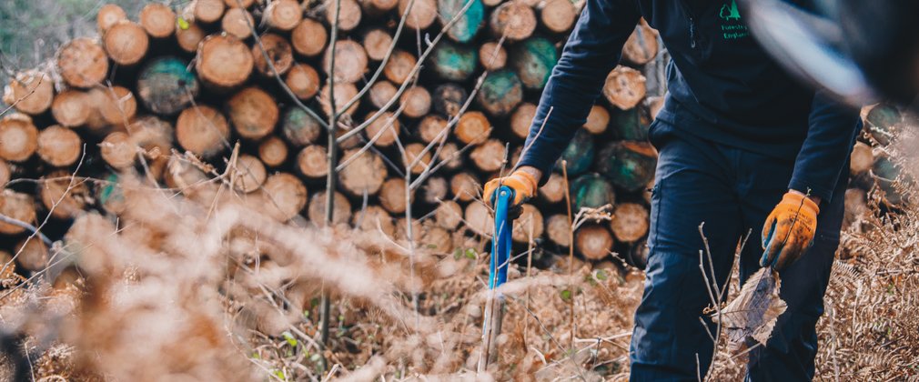 Man digging in front of log pile