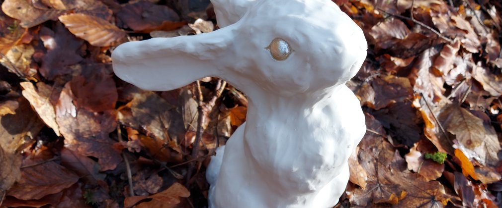 White porcelain rabbit standing on a covering of brown leaves