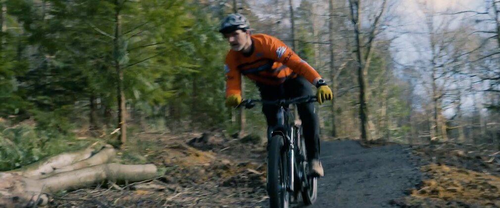 A man in a red top cycling down a forest mountain bike trail