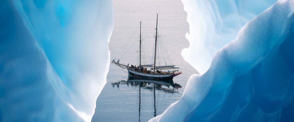 A tall ship with sails down, seen through a gap among ice bergs.