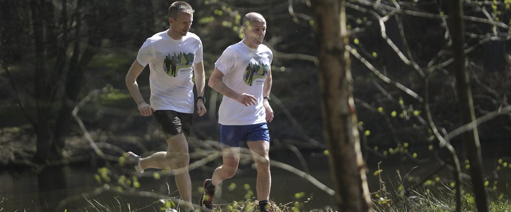 Two men running through the woods on a trail 