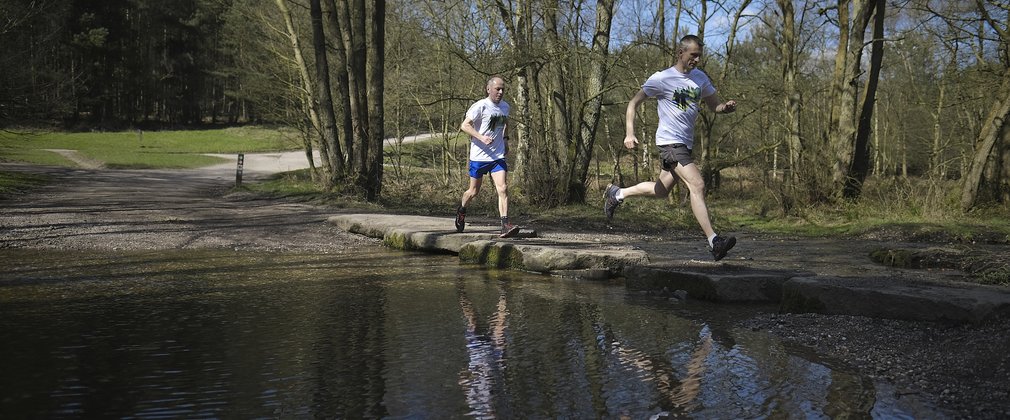 Two men running across stepping stones in a river in the woods 