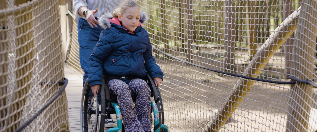 Girl in wheelchair propelling herself up a wooden ramp with nets each side