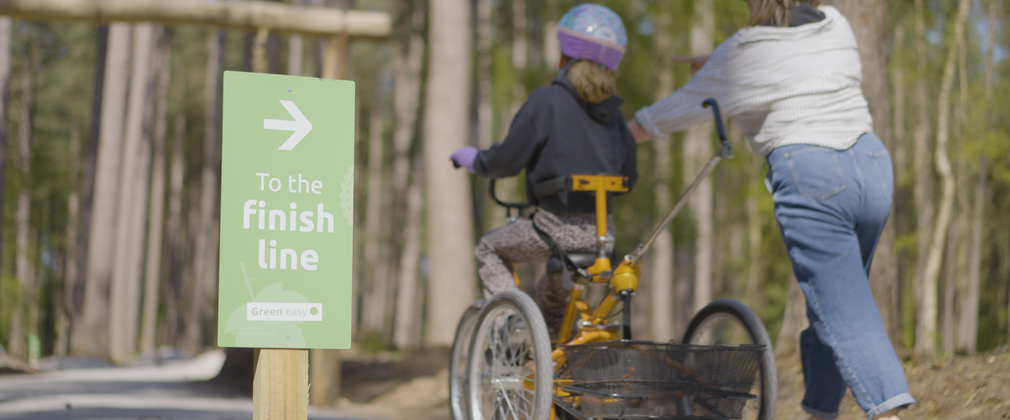 Girl on adapted trike being helped by her mother, riding away to the finish line