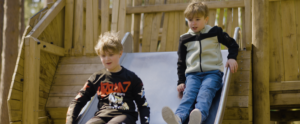 Two boys sliding down a double-width slide together
