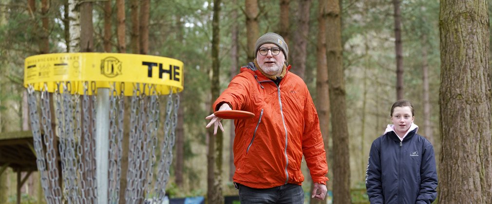 Old bearded man in a green woolly hat and female child playing disc golf
