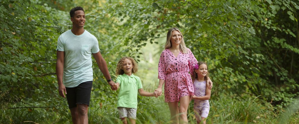 Parents and two children in summer clothes walking in woodland