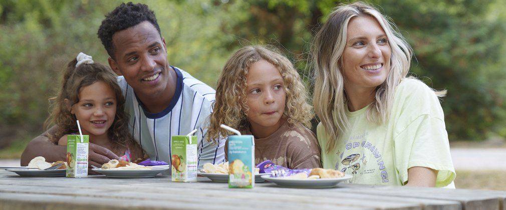 a man and a woman with two children enjoying a picnic in the woodlands