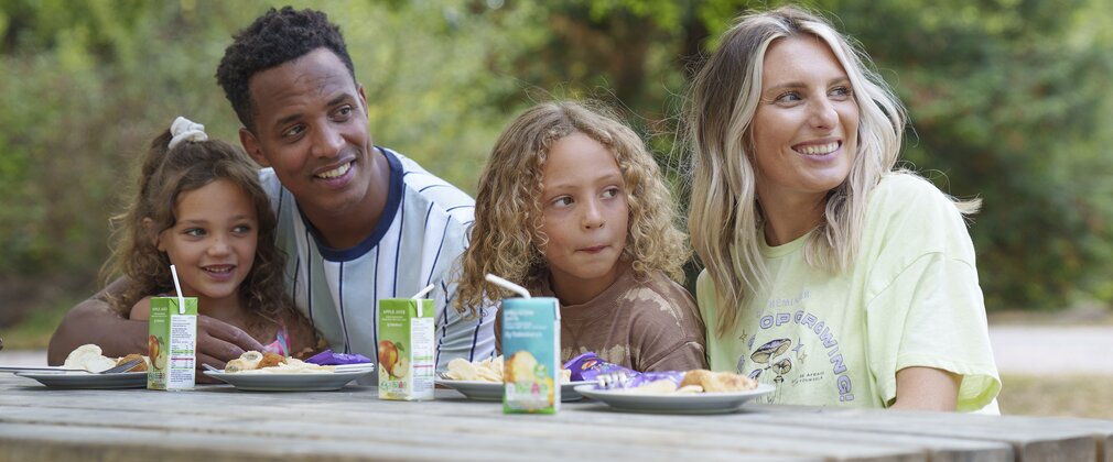 Two parents and two children sitting at a picnic bench with plates of food and drinks