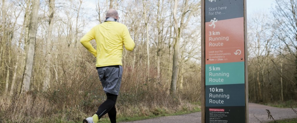 A man running past a sign in the forest wearing a yellow top