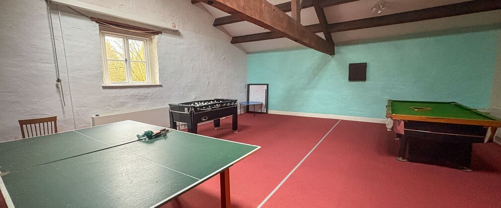 A games room with beamed ceiling, red floor and ping pong table