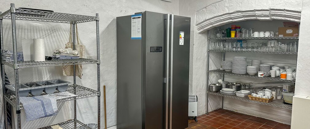 A commercial kitchen with silver American-style fridge and group crockery on shelving