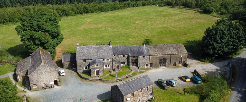 A drone shot of a farmhouse-style building with field and forest behind