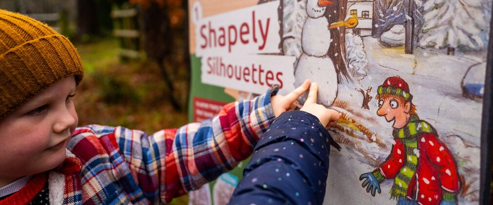 Two children pointing at a Christmas-themed display panel in the forest.
