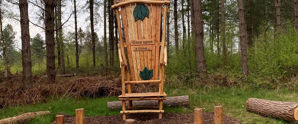 A large wooden chair with once upon a time carved on it, in a forest.