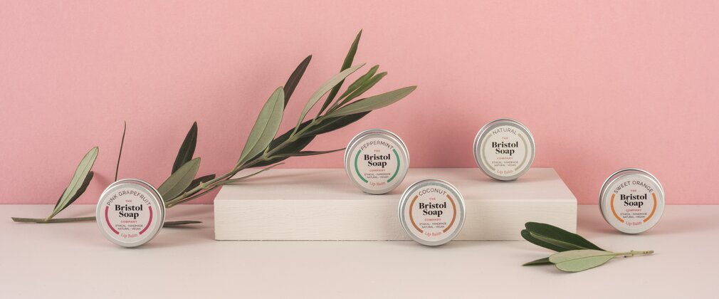 A selection of tin lip balms on display with a pink background