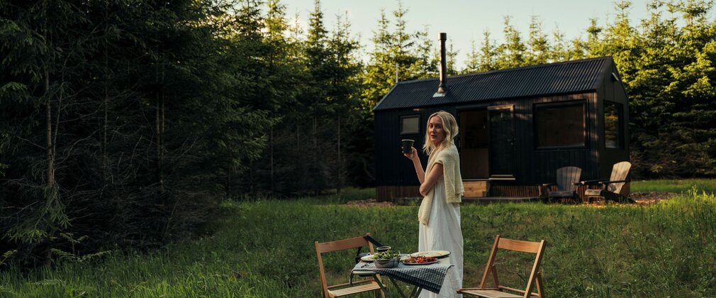 A woman stood outside of a cabin with a dinner set up