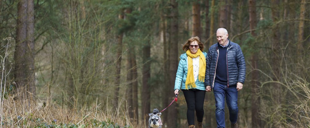 A man and a woman walking on a trail with their small dog on a lead