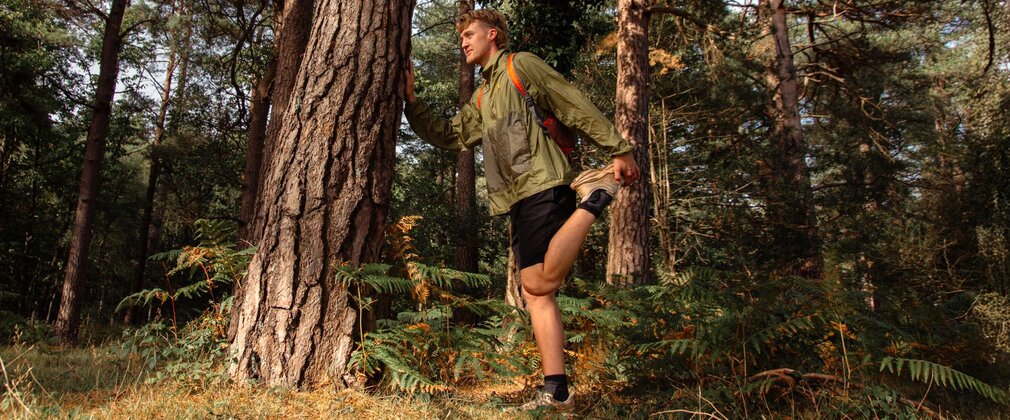 A man leaning against a tree in the forest as he stretches.