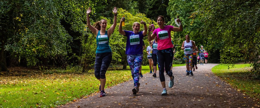 3 runners wave at the camera as they run past in brightly coloured clothes.