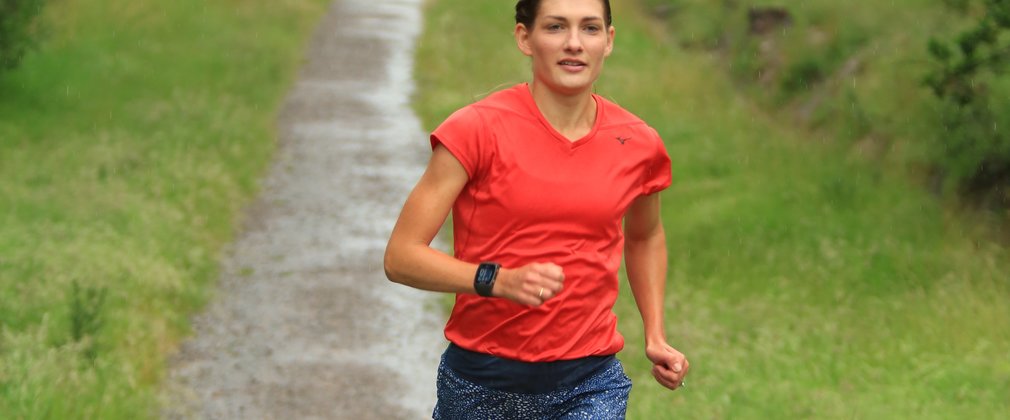 Verity Ockenden in a red jersey running along a woodland path