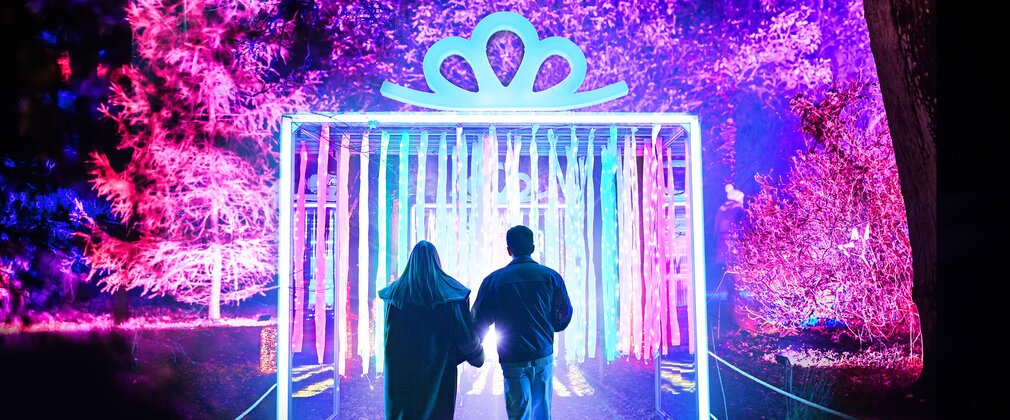 A couple walking under a present installation on an illuminated trail
