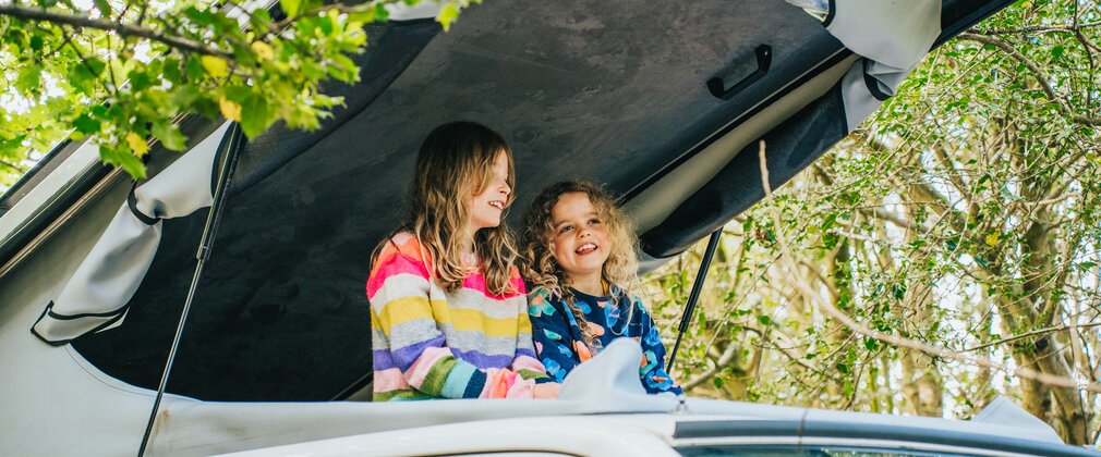 Two girls at the top of a pop top in a campervan