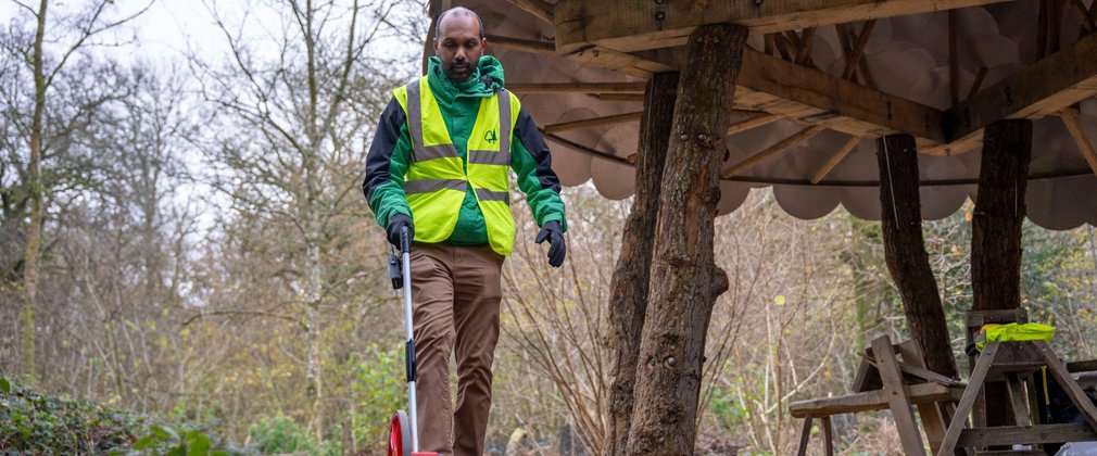 A man wearing Forestry England uniform and a high-visibility using a tool in the forest