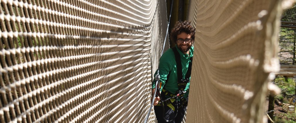 A man smiling whilst travelling through a treetop rope bridge with net sides