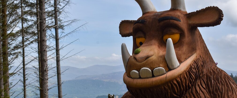 A close up of a Gruffalo sculpture with trees and mountain views behind