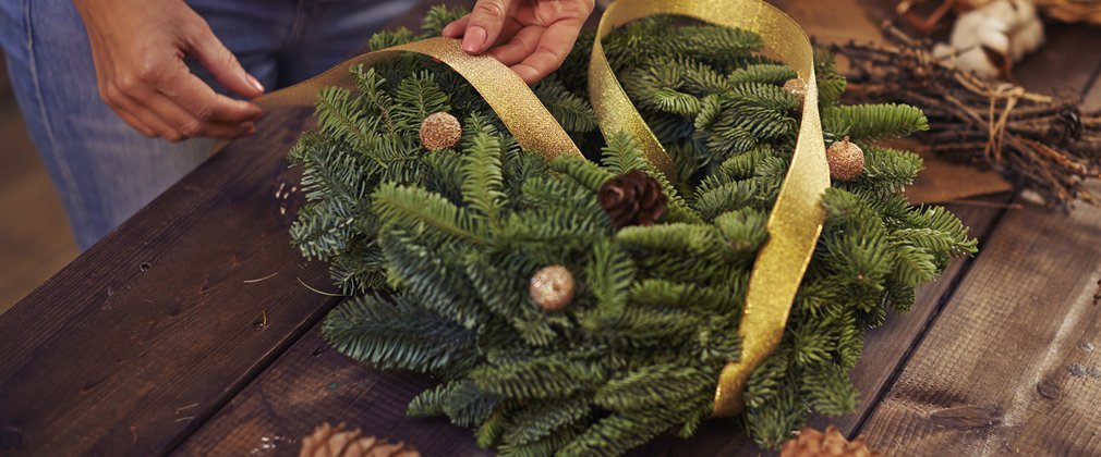 A Christmas wreath in a table with some hands adding a gold ribbon