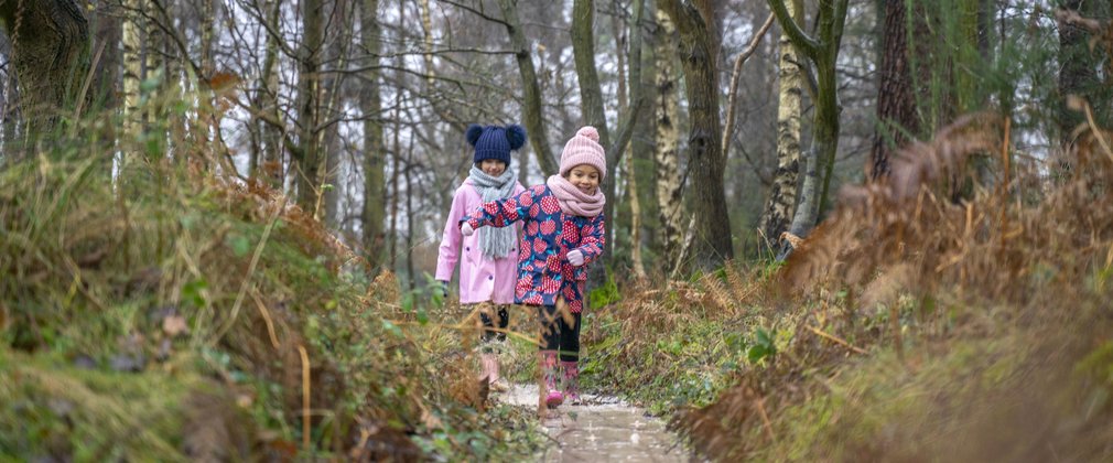 Children walking through a puddle in winter wellies and hats