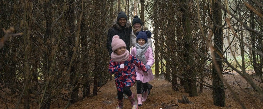 Family running through lines of bare trees in winter