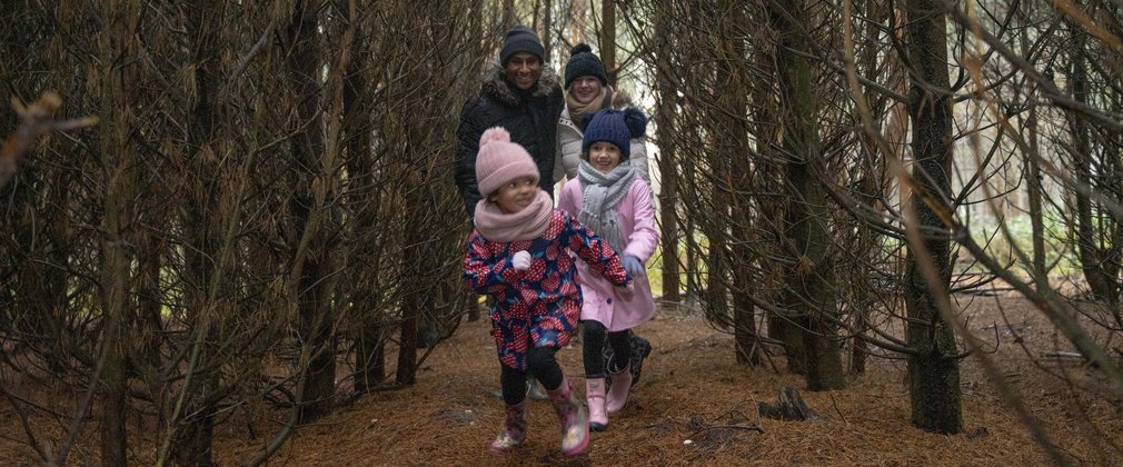 A family running through the trees wrapped up in winter woolies 