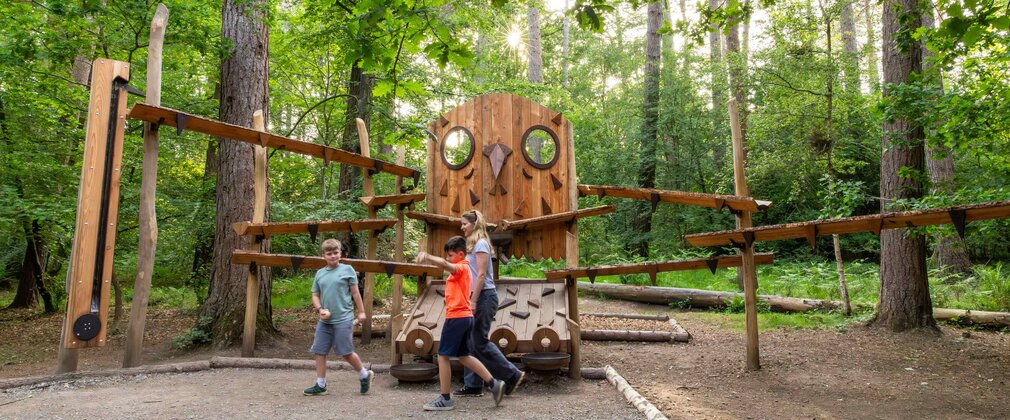 Children with an adult playing on the marble run beside a wooden owl play sculpture at Alice Holt Forest