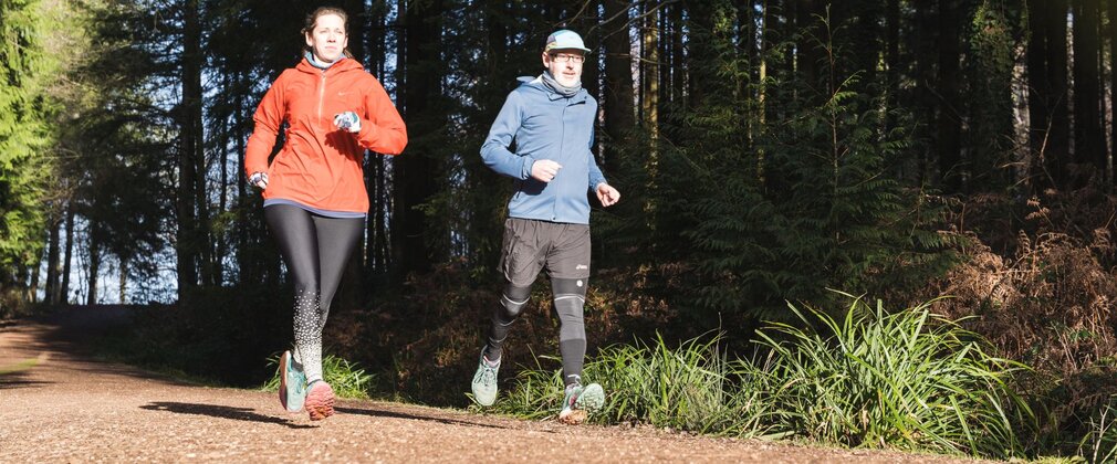 Two people in sports clothing running along a forest path.