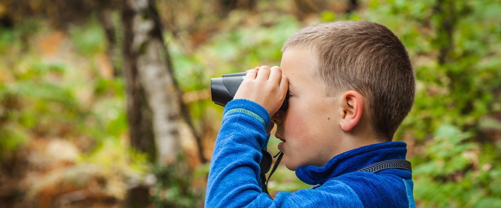 A young boys looks through binoculars in the forest