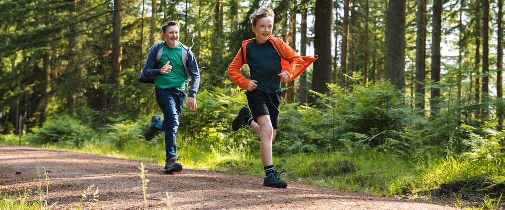 Two boys running along a forest path in the sun.