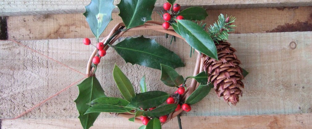 A Christmas wreath made out of green leaves and red berries and a large cone.