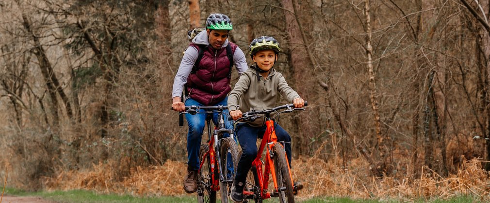 A man and boy wearing cycling helmets cycling on a forest path next to autumn trees