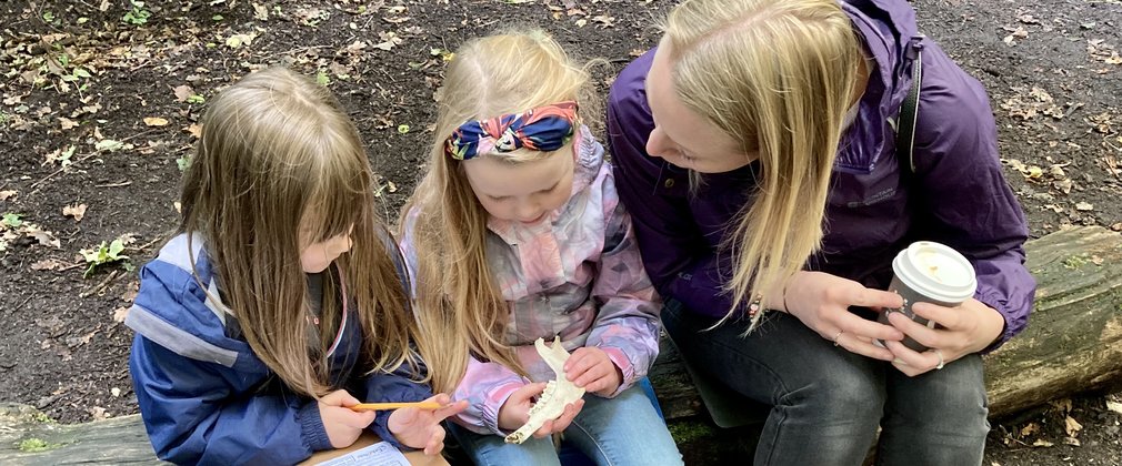 Two children sat on a log with mum.