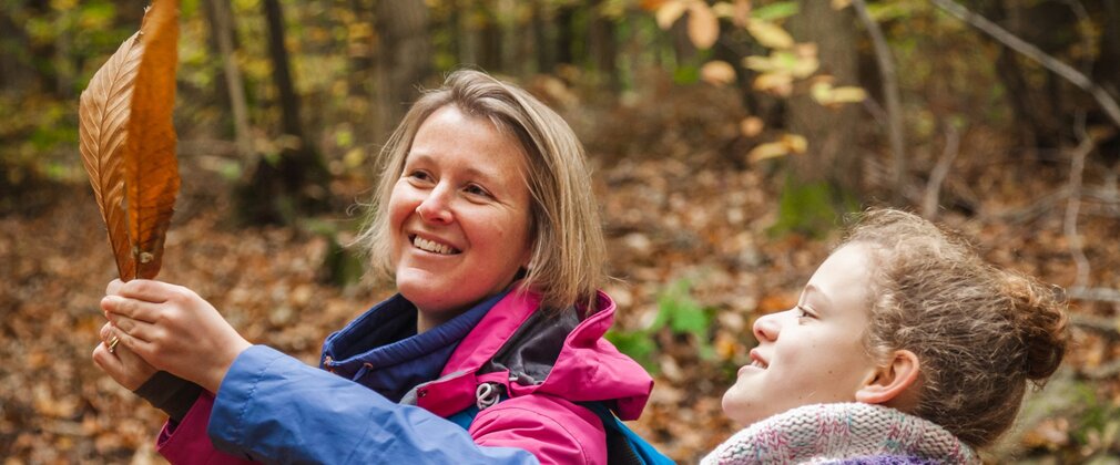A girl and woman looking at a large autumn leaf they've found