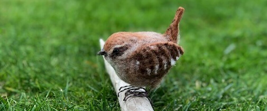A beautiful felted wren sits on a bare branch on grass.