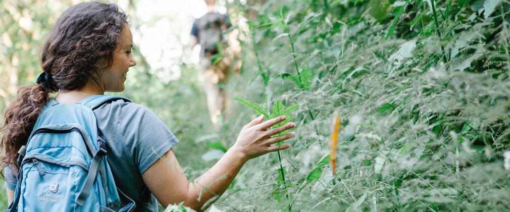A woman smiling as she touches leaves in the forest.