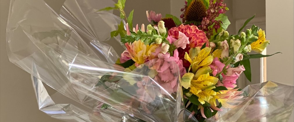 A beautiful bunch of flowers arranged in a brown bag with off cuttings strewn around the table with a pair of yellow secateurs