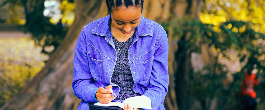 Woman in denim sitting on bench in the forest, writing in a book