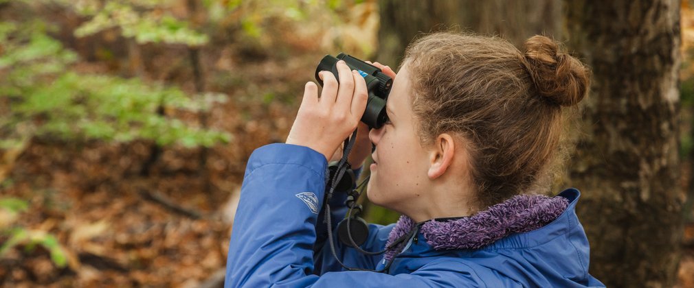 close-up of a girl looking through binoculars in the forest