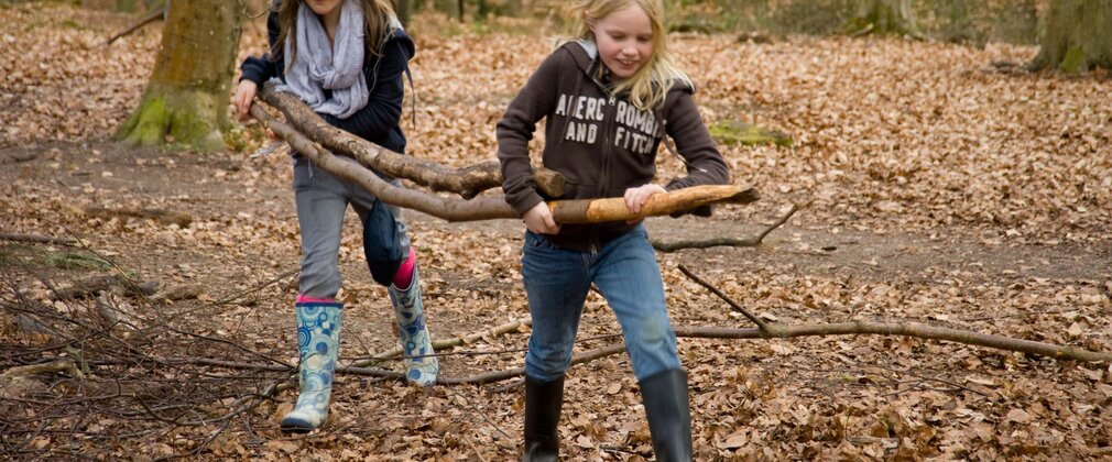 Two girls carrying branches to build a den in the woods 