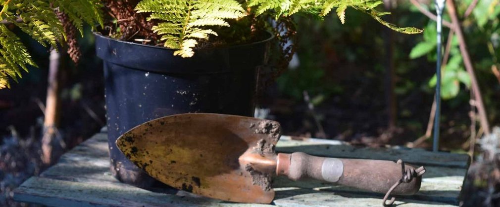 A trowel sits on it's side resting against a plant pot. The trowel is shaped like an arrow and has dirt around the edge.