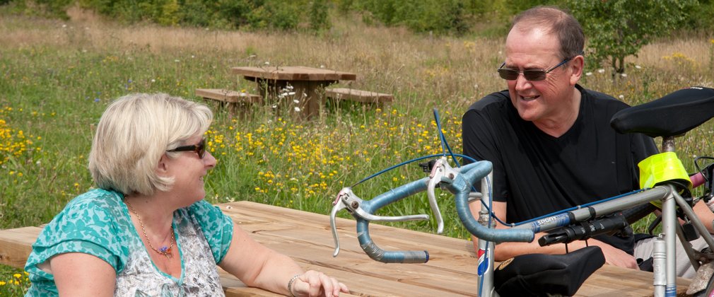 middle aged couple with bicycles by a picnic bench
